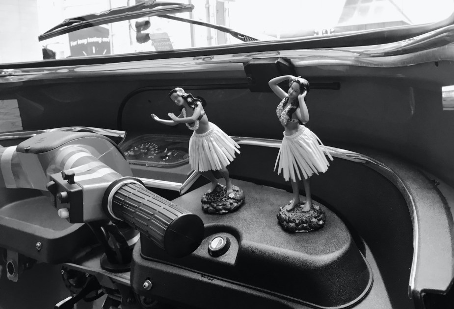 Black and white photos of a Hula girl figurine next to the handlebars of a vehicle.