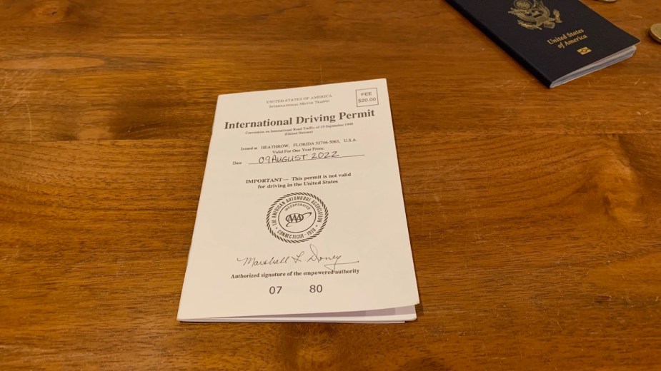 An International Driving Permit booklet on a wooden table with a passport booklet visible in the background.