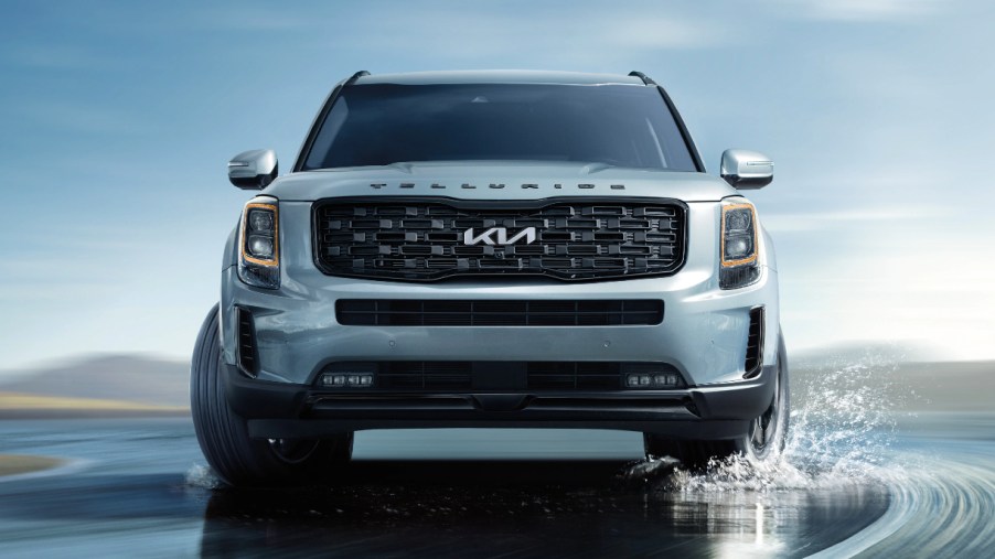 A gray 2022 Kia Telluride midsize SUV is driving on a wet road.