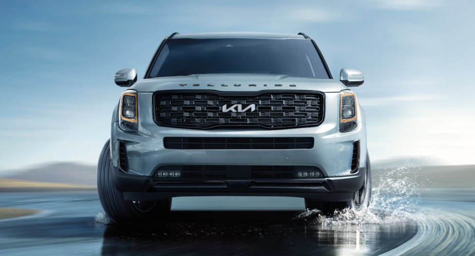 A gray 2022 Kia Telluride midsize SUV is driving on a wet road. 