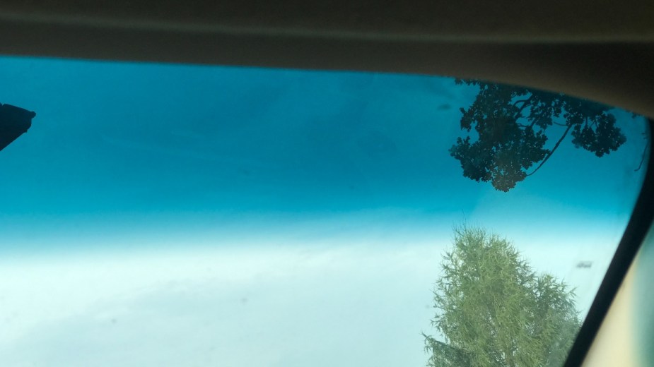 Car windshield with a blue-green color-tinted layer at the top, and a tree in the background