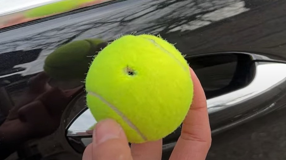 Man holding tennis ball by car door, highlighting if you can unlock a car door with a tennis ball