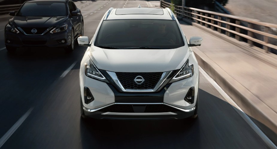 Two Nissan Murano midsize SUVs are driving on the road. 