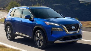 A blue 2022 Nissan Rogue compact SUV is driving on the road.