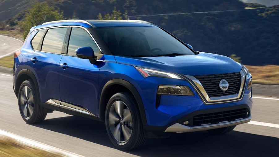 A blue 2022 Nissan Rogue compact SUV is driving on the road.