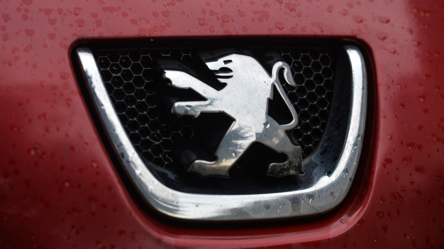 Closeup of a lion car logo set into the small grille of a red car, rain drops visible on its paint.