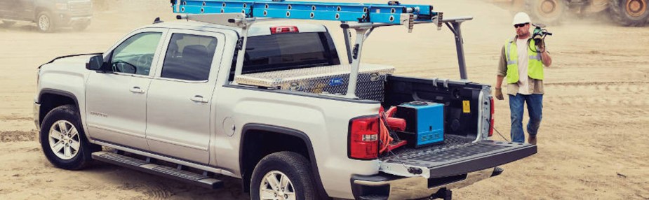 Pickup truck on a jobsite modified with a ladder rack and crossover-style in bed toolbox.