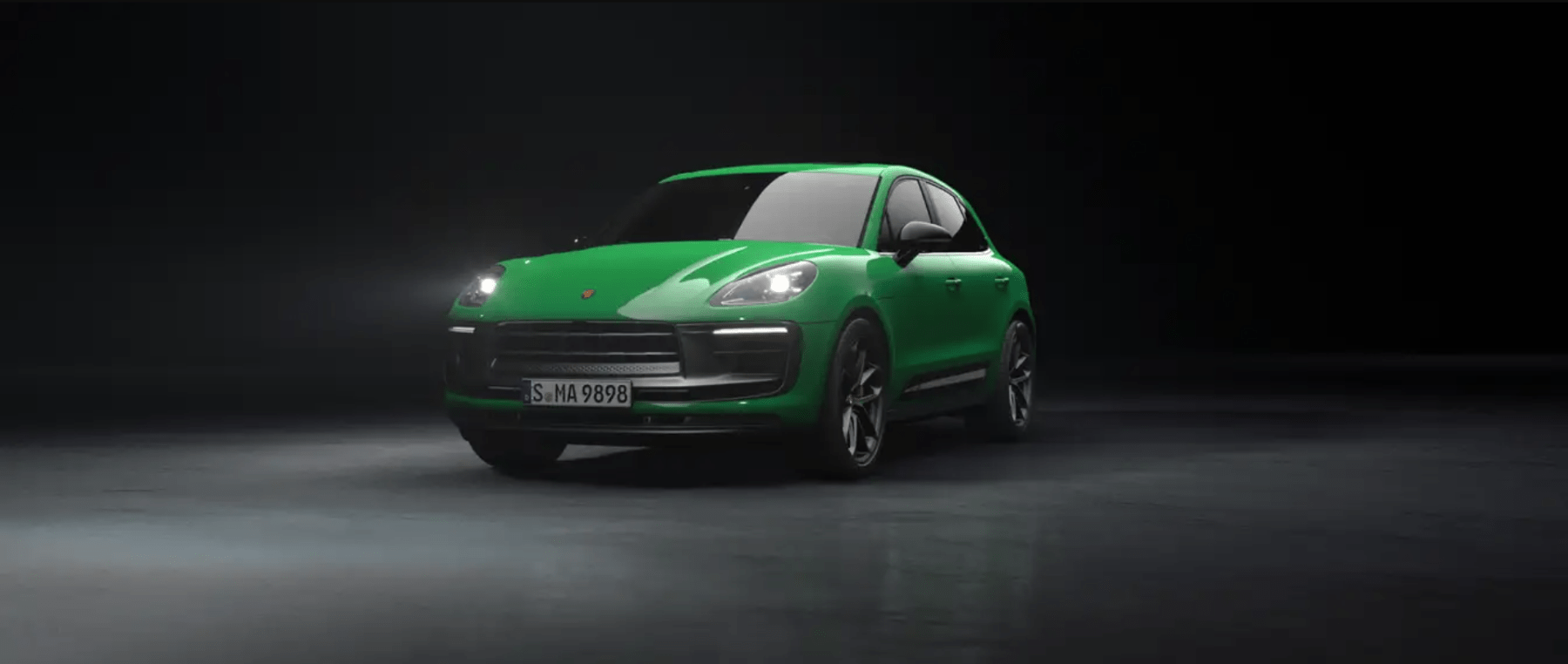 A green 2023 Porsche Macan luxury compact SUV promotional photo in a dark black void