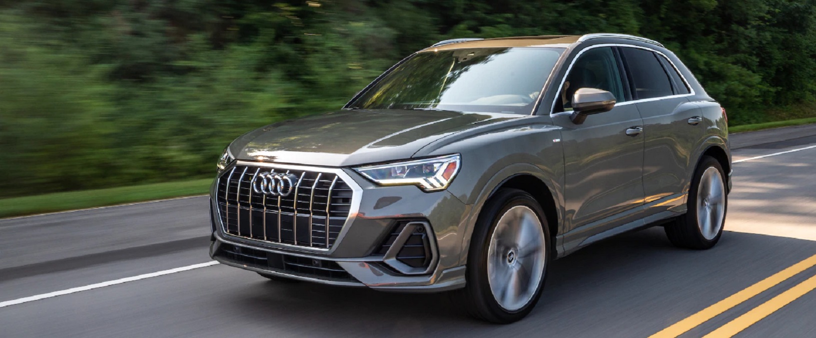 A gray 2022 Audi Q3 driving down a tree-lined road.