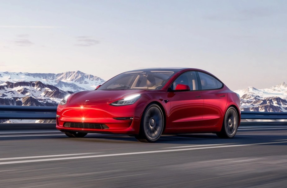 Red 2022 Tesla Model 3 driving by mountains, highlighting why luxury cars have boring letter and number names