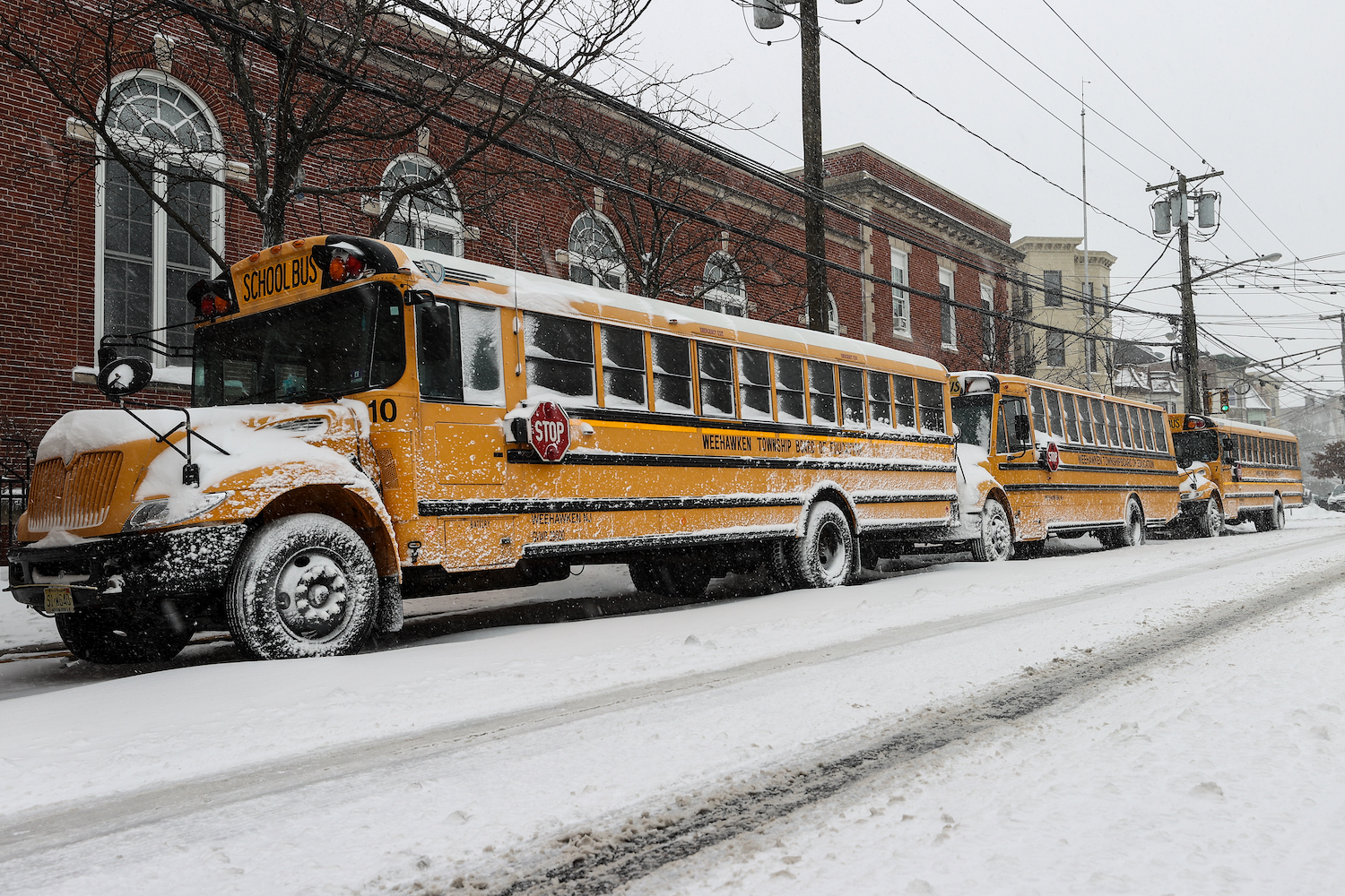 A row of school buses parked on a snowy street in poor weather.
