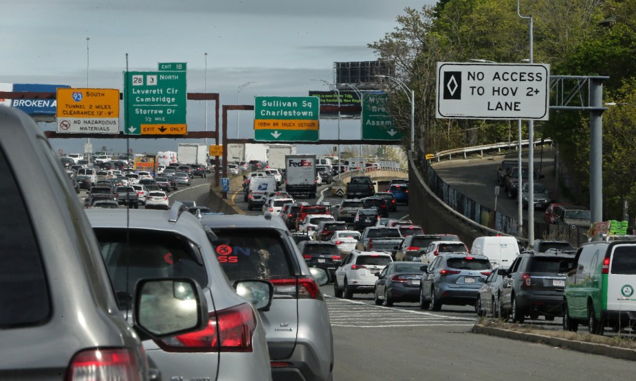 A Boston highway packed with standstill traffic, exit signs for Cambridge visible in the background.