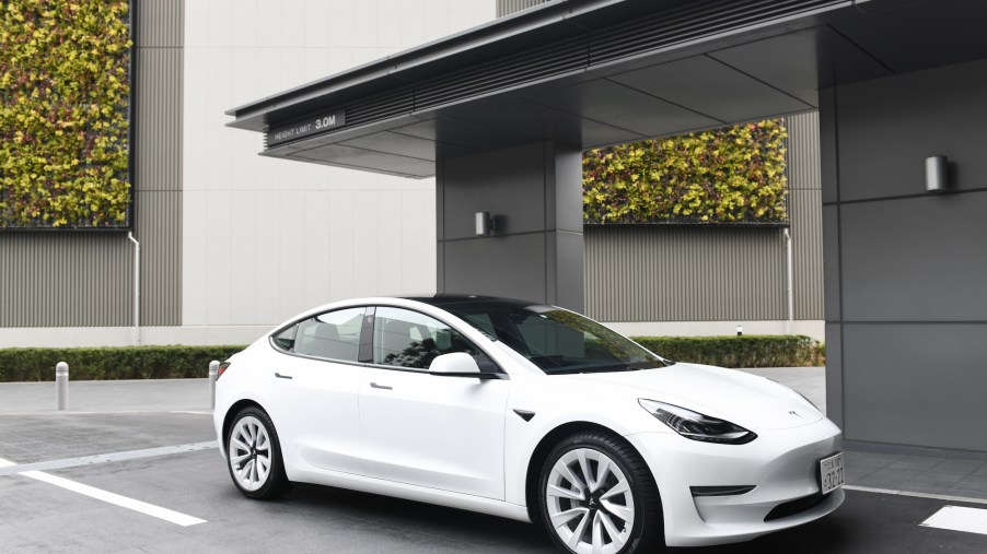 A white Tesla Model 3 in front of a black and white building.