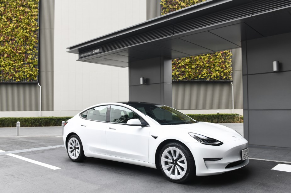 A white Tesla Model 3 in front of a black and white building.