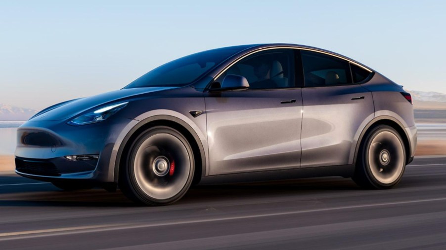 A gray Tesla Model Y electric SUV is driving on the road.
