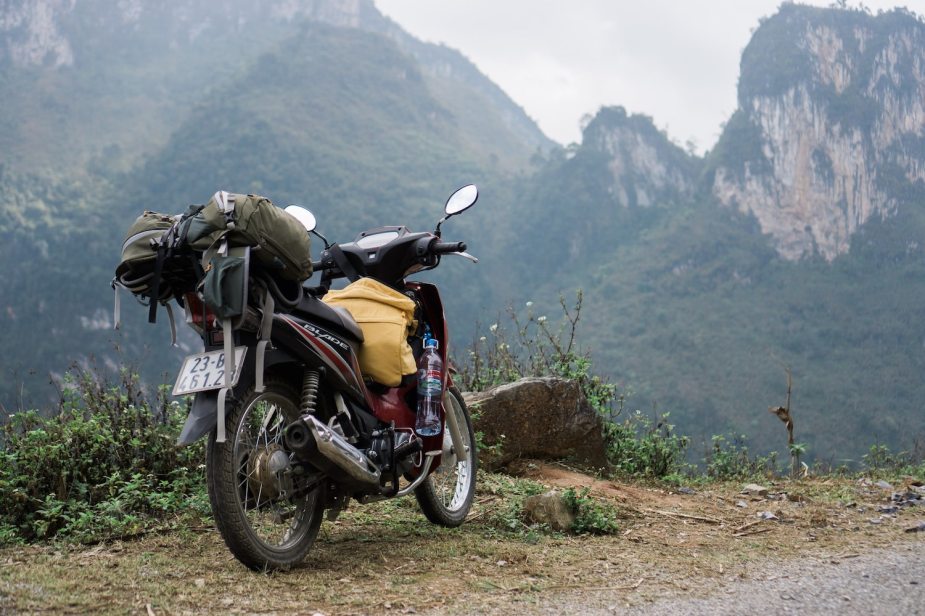 An on/off-road motorcycle parked in the mountains, a backpack lashed to its luggage rack.