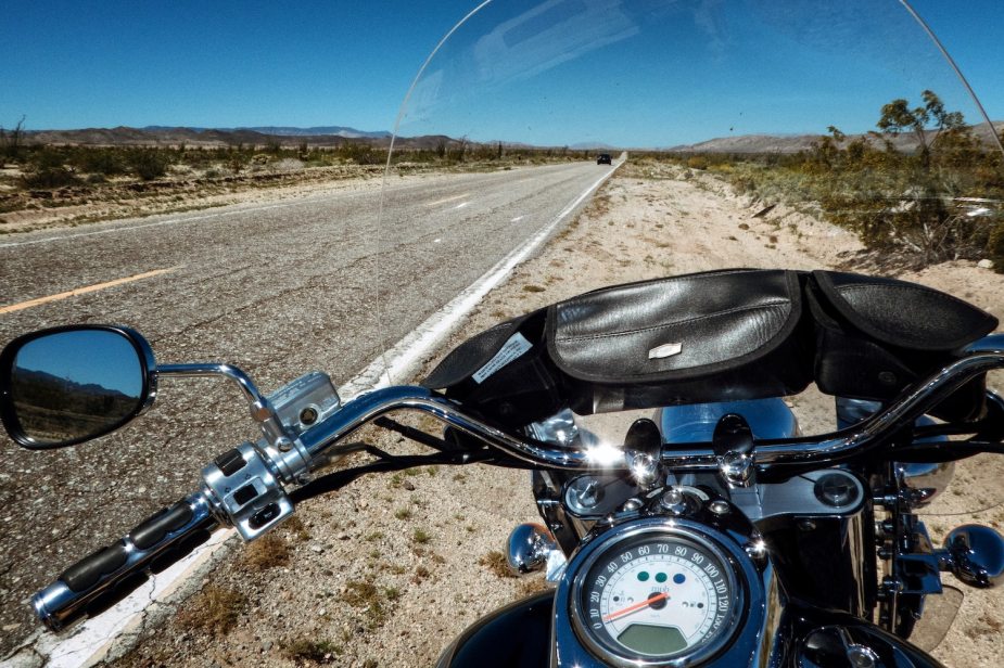 The view of a desert road from behind a motorcycle's windshield and handlebars.