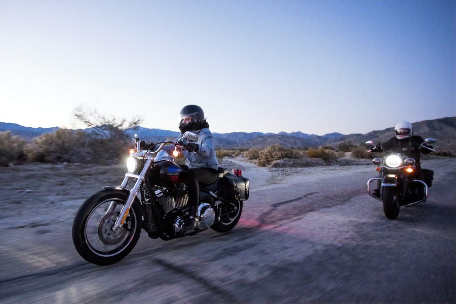 Photo of two motorcyclists riding Harley Davidsons along a paved road at twilight.