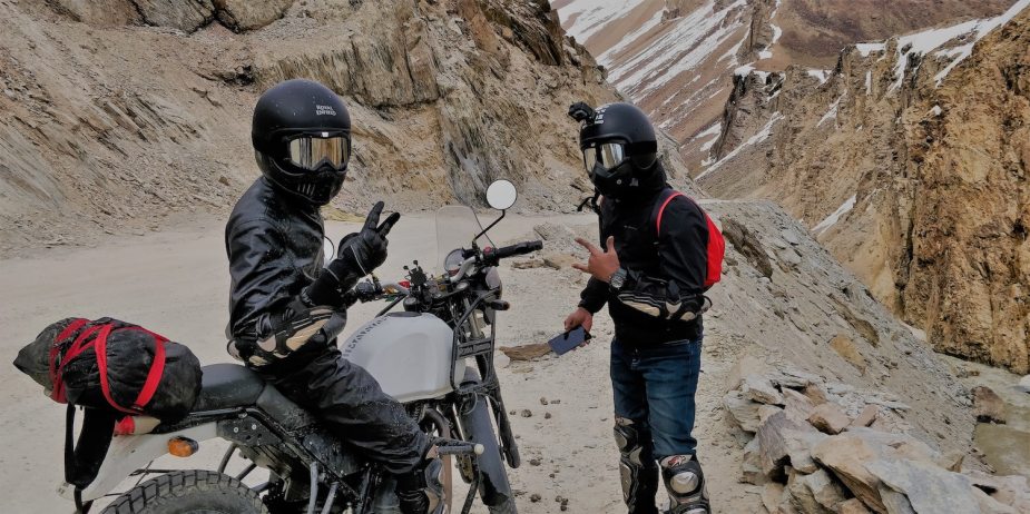 Two ultralight motorcycle travelers stop on a mountain road to take a photo during their camping road trip.