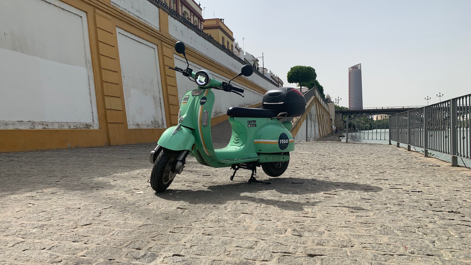 Picture of a retro, app-based electric rental scooter offered by the European YEGO company, with a stone wall visible in the background.