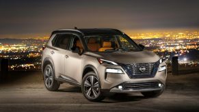 A bronze 2022 Nissan Rogue compact SUV model parked on a hill above a city of lights at night