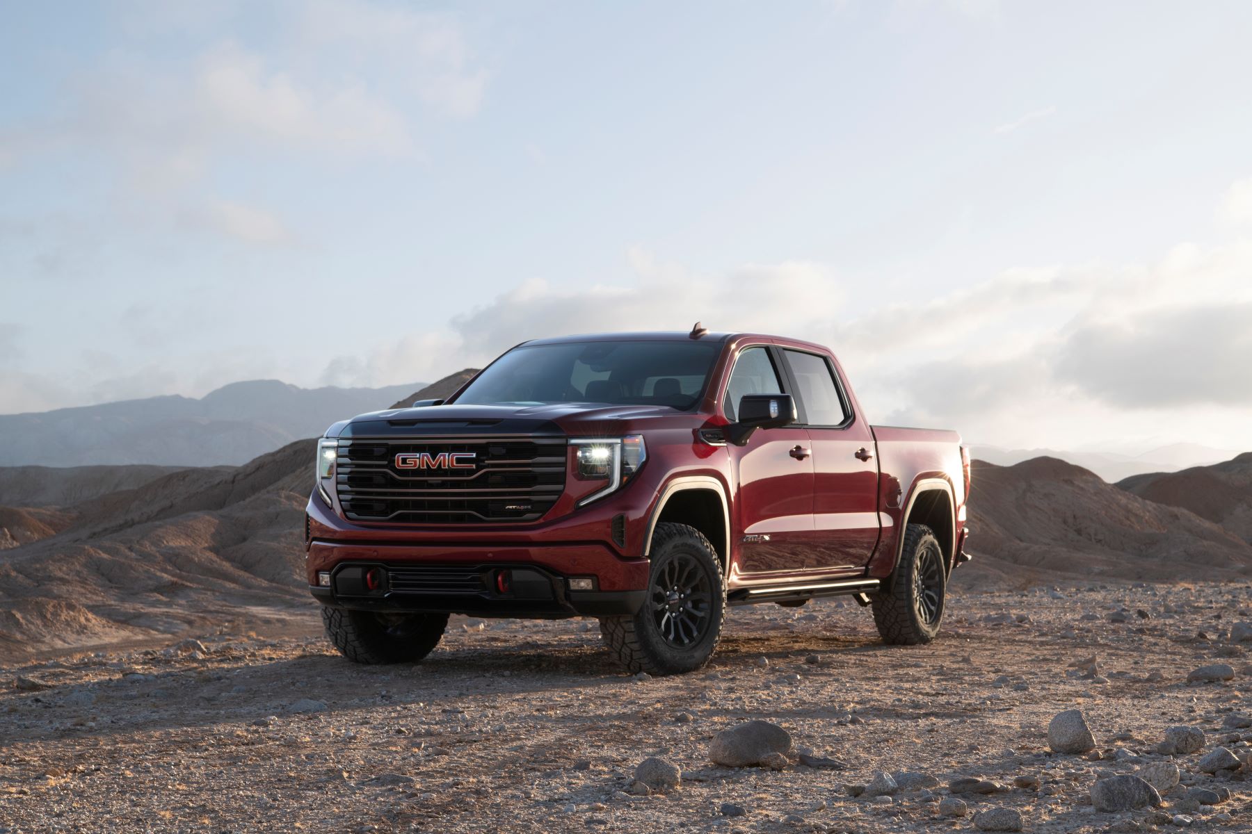 A red 2022 GMC Sierra 1500 AT4X full-size pickup truck model parked on a dirt plain amidst hills and mountains
