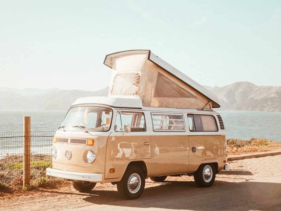 Tan colored VW Bus parked by the ocean, its camper top popped up.