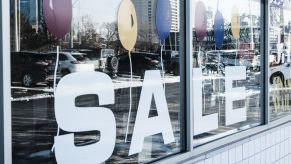 A used car dealership window 'SALE' sign and reflection of models on the lot in Detroit, Michigan