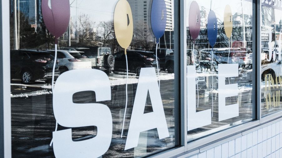 A used car dealership window 'SALE' sign and reflection of models on the lot in Detroit, Michigan