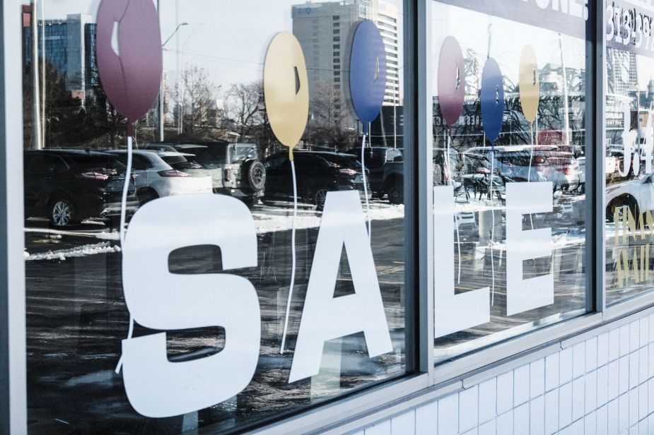 A 'SALE' used car dealership window sign and reflection of models on the lot in Detroit, Michigan