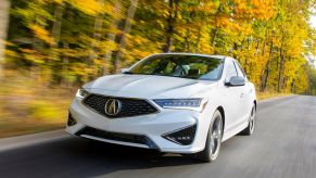 A white 2021 Acura ILX A-Spec compact luxury sedan/executive car driving near a yellow leaf forest of trees
