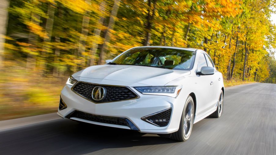 A white 2021 Acura ILX A-Spec compact luxury sedan/executive car driving near a yellow leaf forest of trees