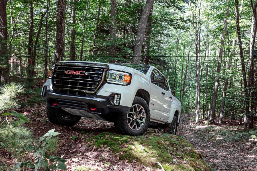 A white 2022 GMC Canyon AT4 midsize truck model (available in diesel) traveling off-road through a forest