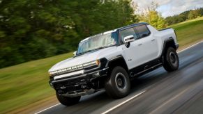 A white GMC Hummer EV pickup truck model speeding down a country highway