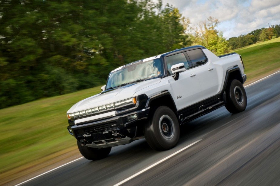 A white GMC Hummer EV pickup truck model speeding down a country highway