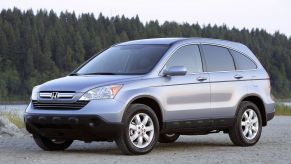 A silver gray 2007 Honda CR-V EX-L with Navigation compact SUV model parked on sand near a river and forest