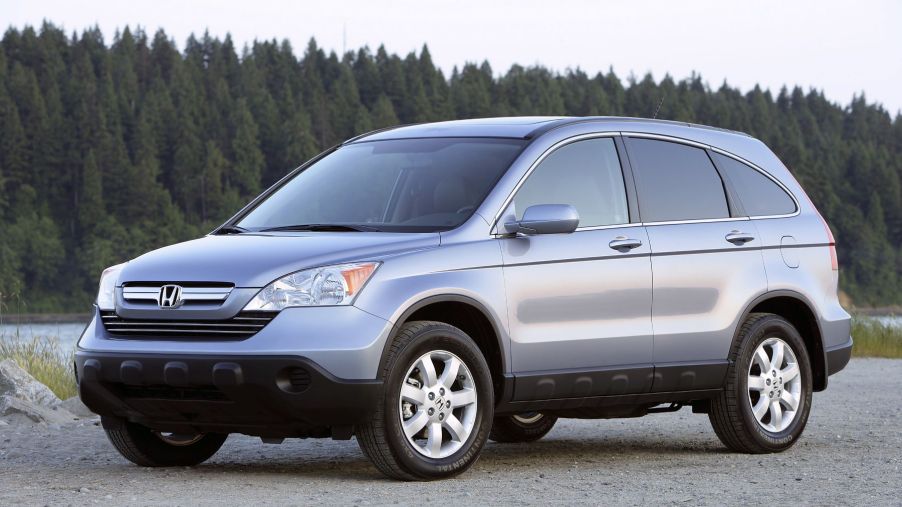 A silver gray 2007 Honda CR-V EX-L with Navigation compact SUV model parked on sand near a river and forest