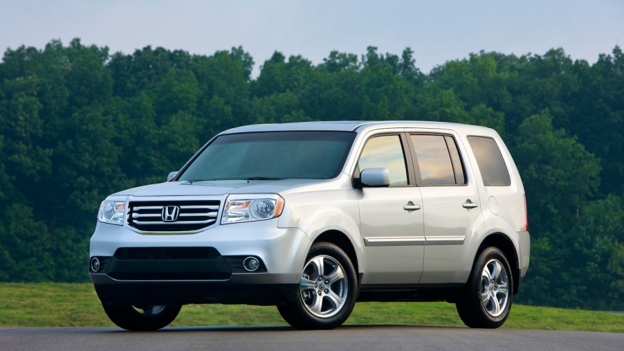 A silver 2015 Honda Pilot parked in front of trees, the Pilot is one the safest used SUVs for teens
