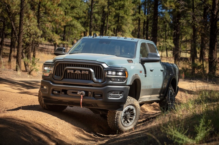 75th anniversary gray-blue Ram 2500 power wagon truck parked on an off-road trail between pine trees, demonstrating how far its suspension flexes.