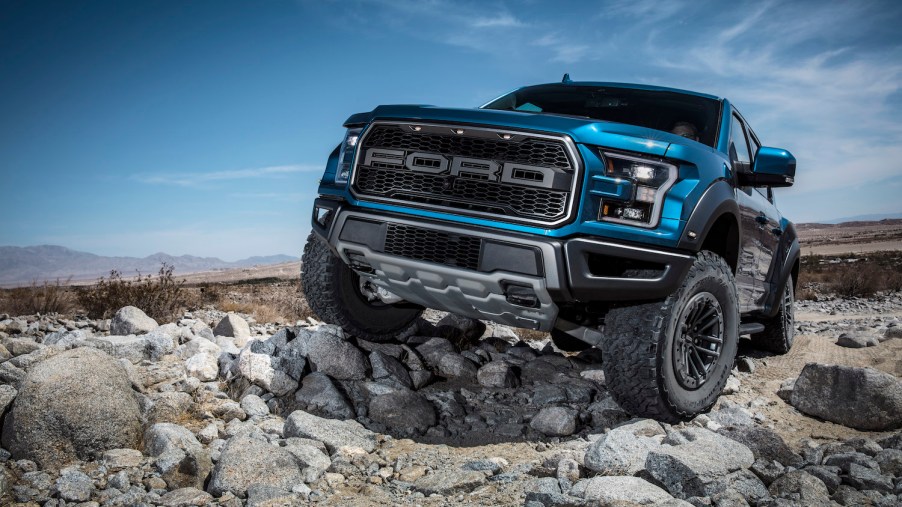 Promo photo of a blue 2021 Ford F-150 Raptor pickup truck parked on a rock-strewn off-roading trail.
