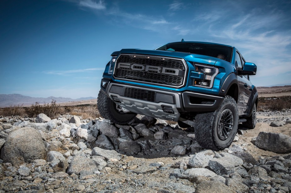 Promo photo of a blue 2021 Ford F-150 Raptor pickup truck parked on a rock-strewn off-roading trail.
