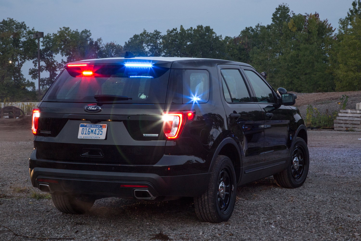 The back of a black Ford police SUV without the badge with a row of trees visible in the background.