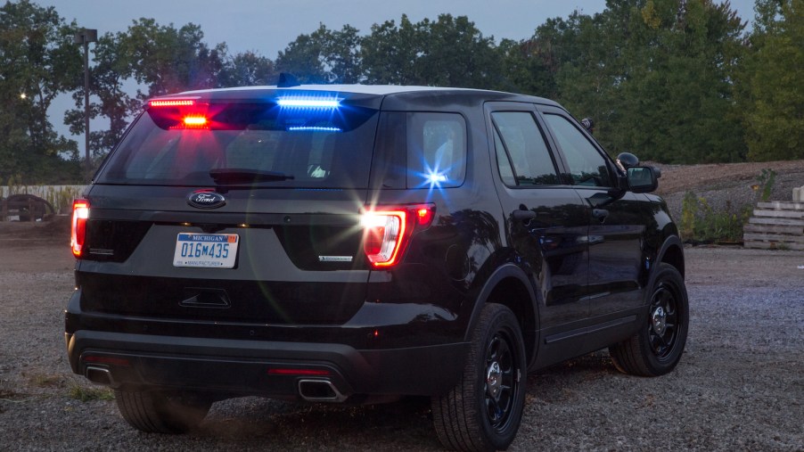 The rear of a black, unbadged Ford police SUV with a row of trees visible in the background.