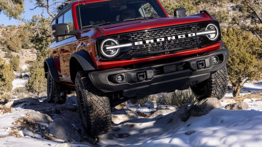 A red 2022 Ford Bronco Wildtrak off-road compact SUV driving on snow-covered rocks