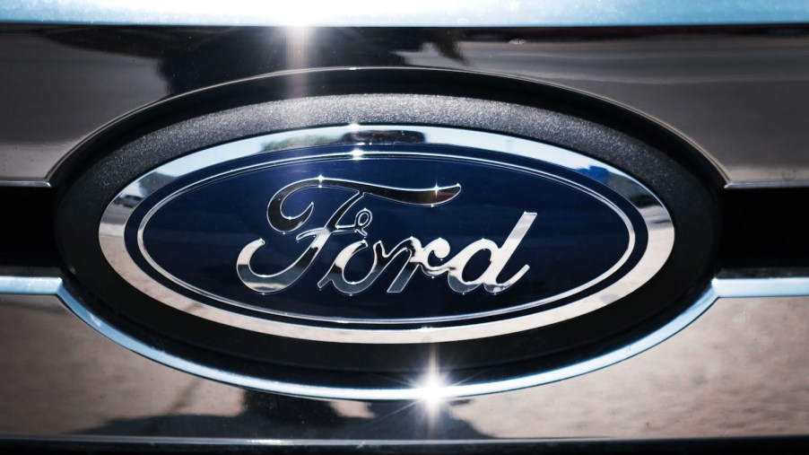 Closeup of Ford's Blue Oval logo in the chrome grille of a hybrid PowerBoost F-150 pickup truck.