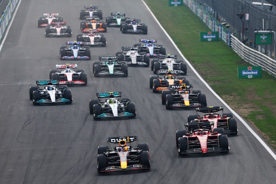 A pack of Formula 1 cars accelerating from the start line of a race track during a grand prix.