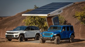 Two Jeep hybrid SUVs plugged into a remote solar panel, shrubs and the desert visible behind them.