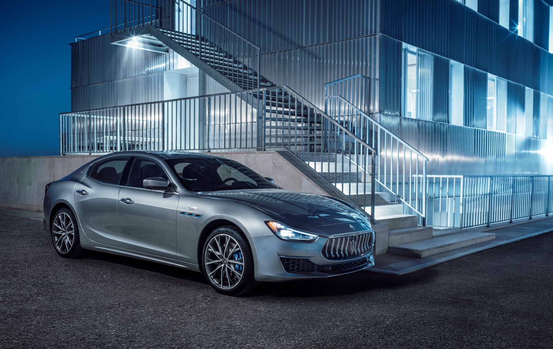 A gray 2022 Maserati Ghibli GT executive car/luxury sedan parked next to metal stairs and fencing at night