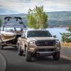 A bronze 2022 Nissan Frontier compact pickup truck towing a speedboat near a lake