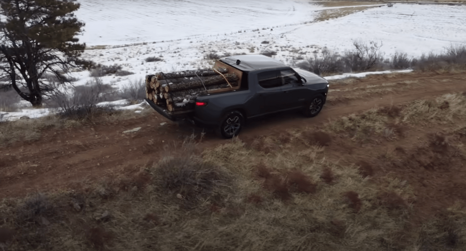 Rivian electric truck hauling a load of logs down the side of a snowy mountain.